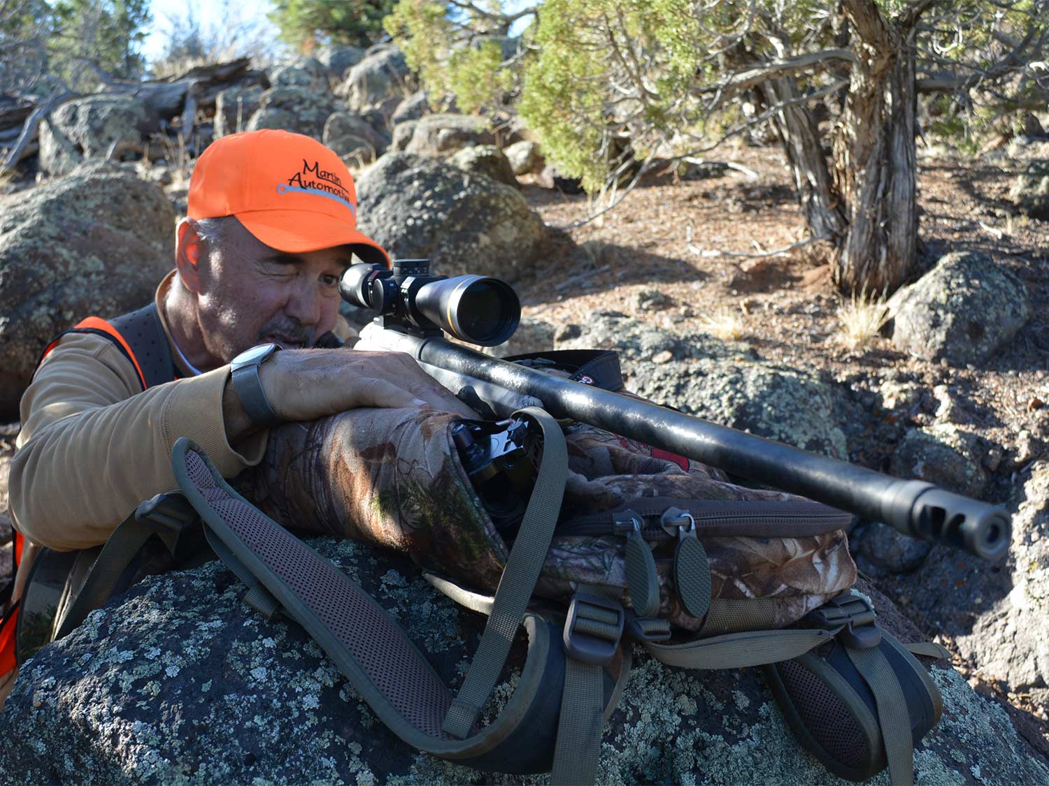 A man aims a rifle in the wilderness.