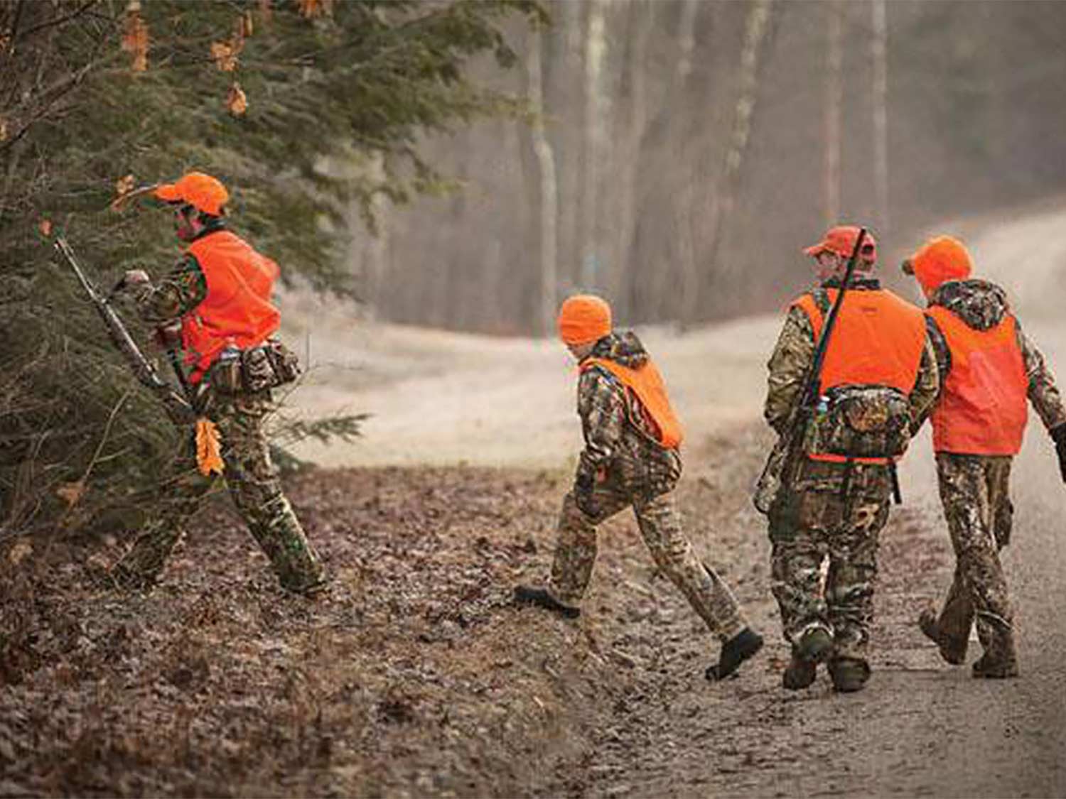 A group of hunters walk through rustling leaves into a tree line.