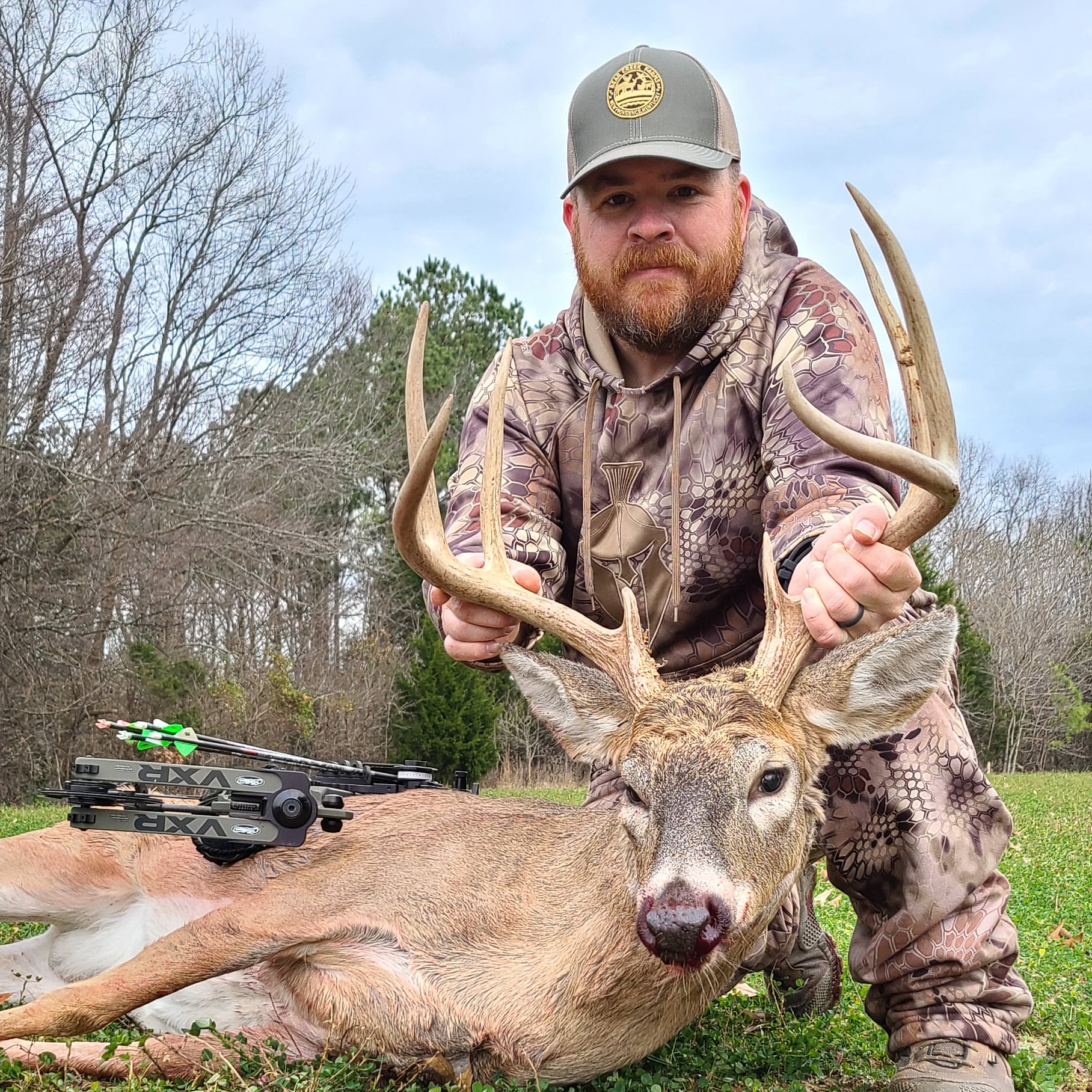 A bowhunter in kyrptek camo holds the antlers of a nice Kentucky buck.
