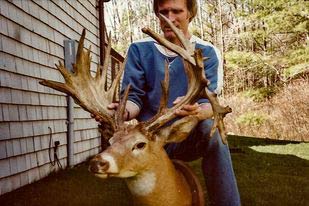 A hunter kneeling behind a large whitetail deer trophy.