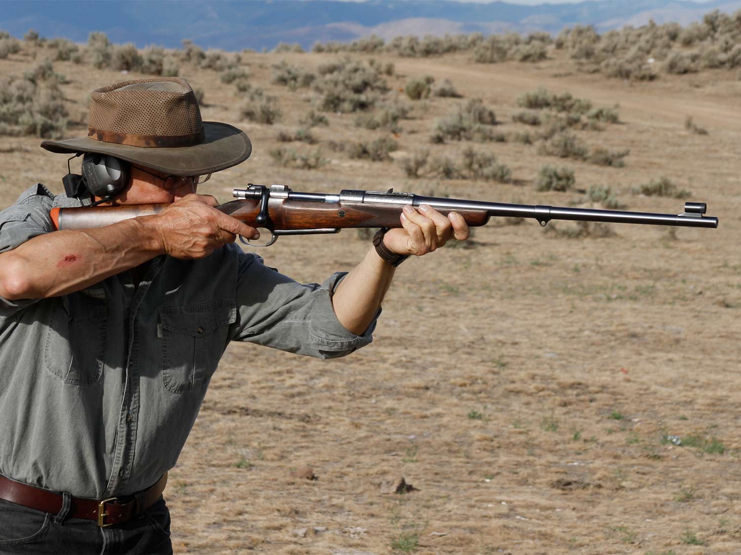 A hunter aims a rifle on an African plain.