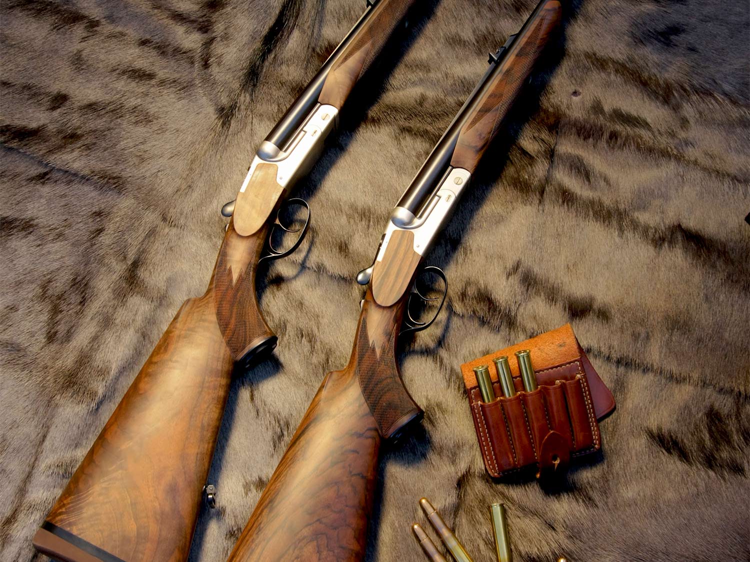 Two hunting rifles on a pelt with ammo beside them.