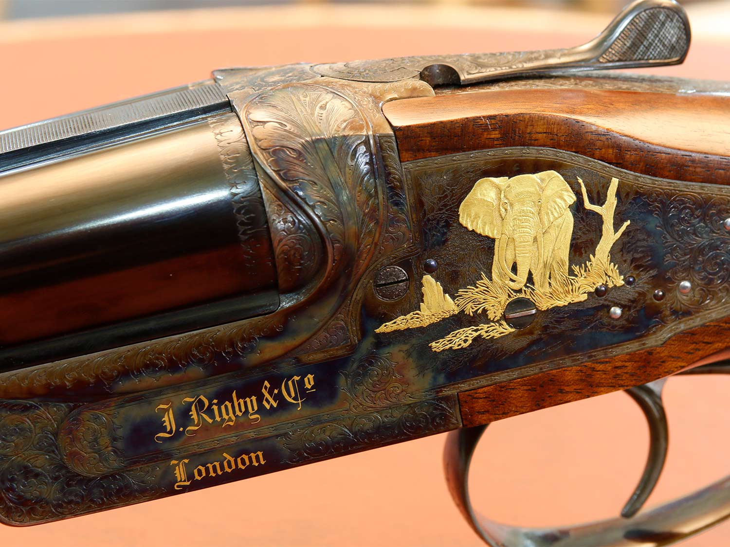 Closeup detail of a rifle stock showing custom engraving and an elephant inlay made of gold.