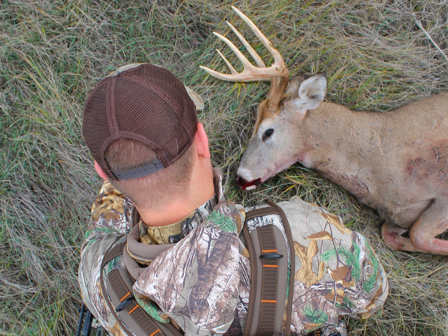 A hunter sits next to a whitetail deer that's dead on the ground.