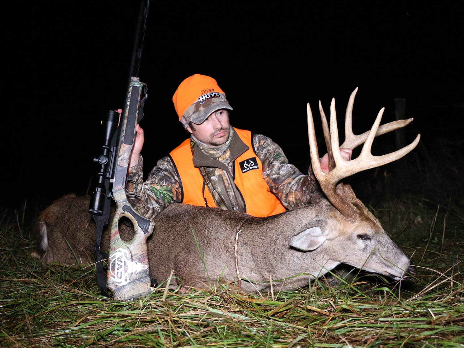 A hunter sits next to a whitetail deer and holds its head by the antlers.