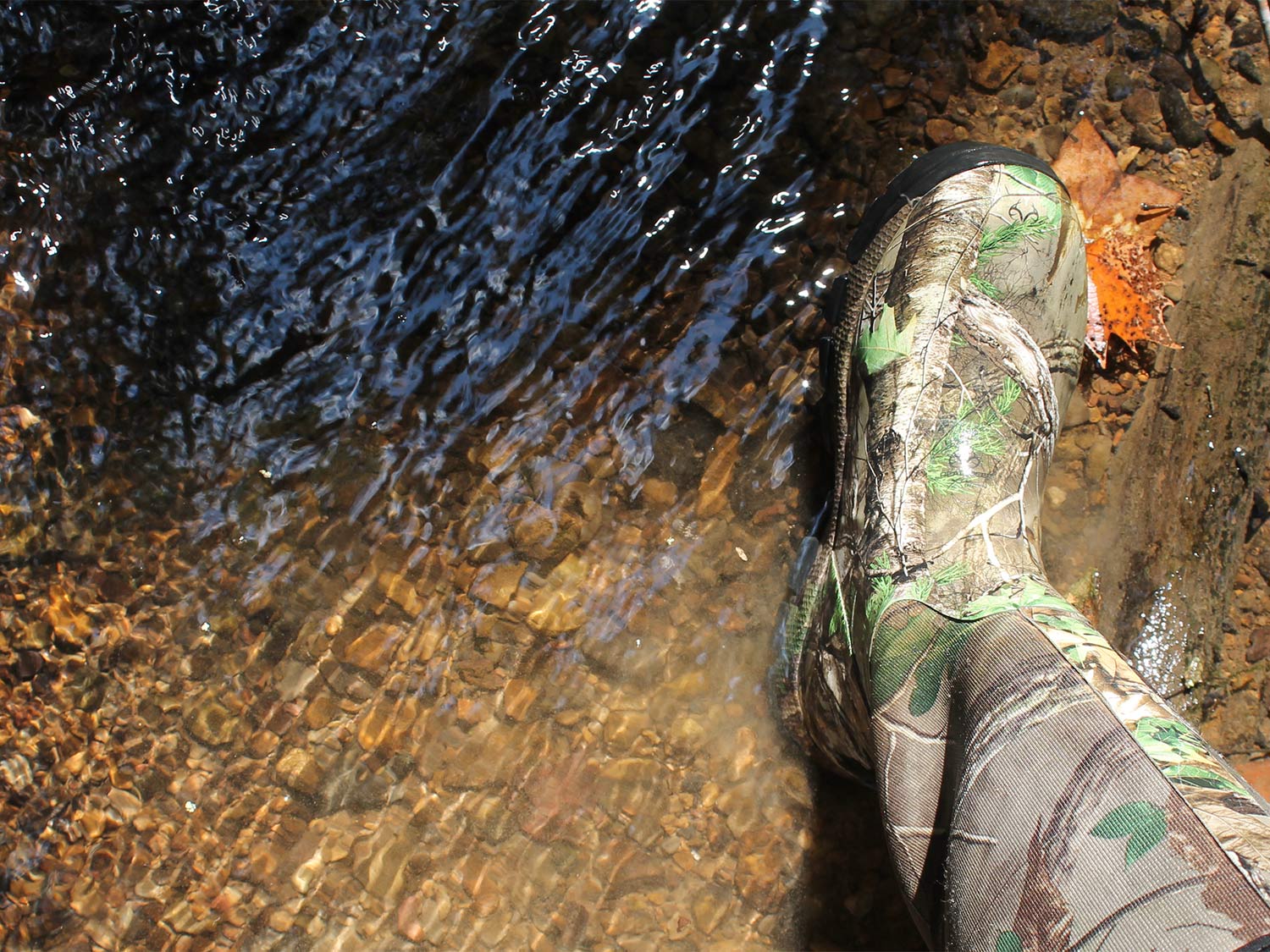 A hunters foot in wading boots is next to water.