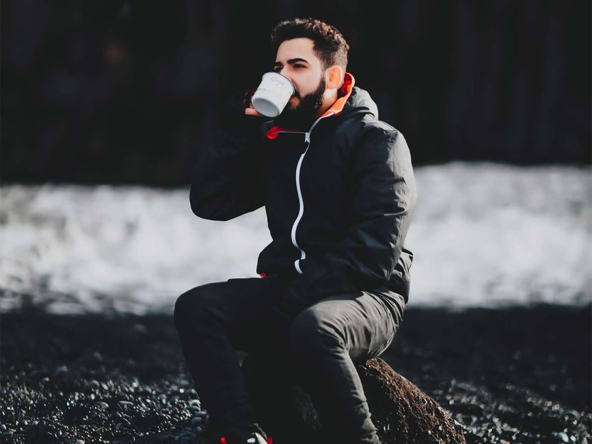 A man sits in the woods and drinks coffee.