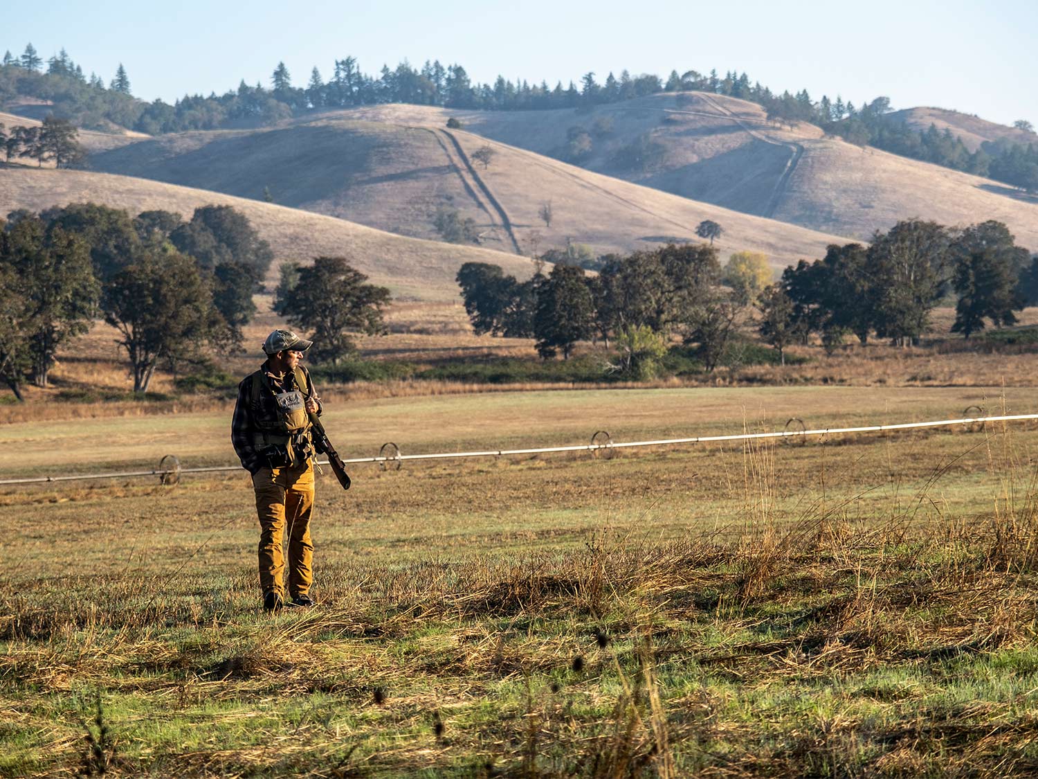 A hunter walks through a large open field.