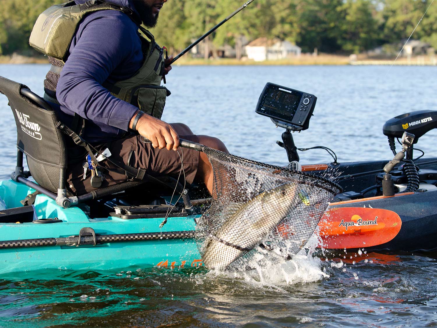 An angler pulls a fish into a kayak using a net.