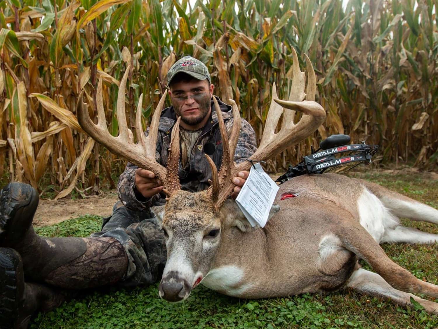 A bow hunter sits behind a big Ohio buck and holds its head by the antlers.