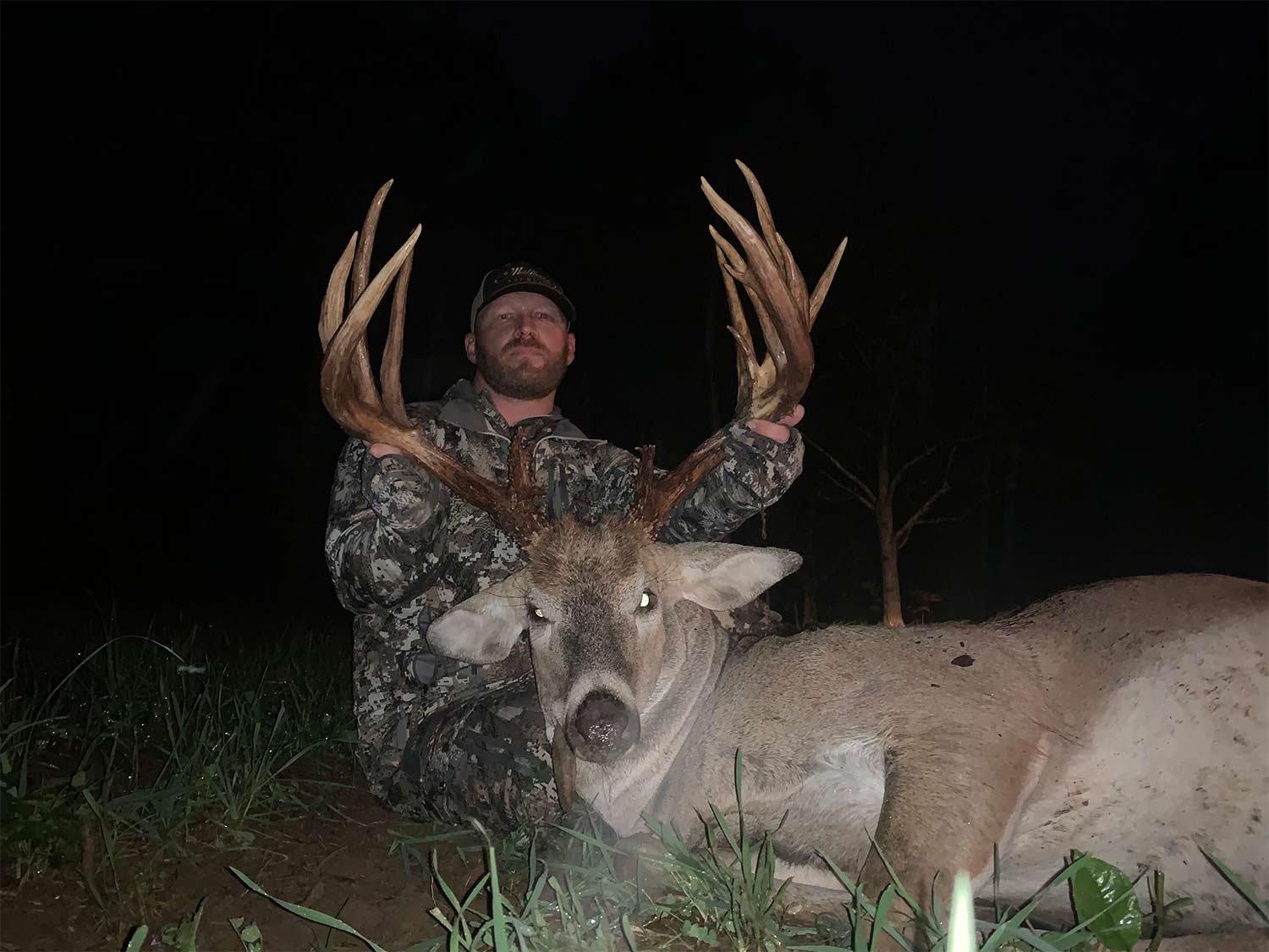 A bowhunter sits behind a big-bodied whitetail buck after dark.