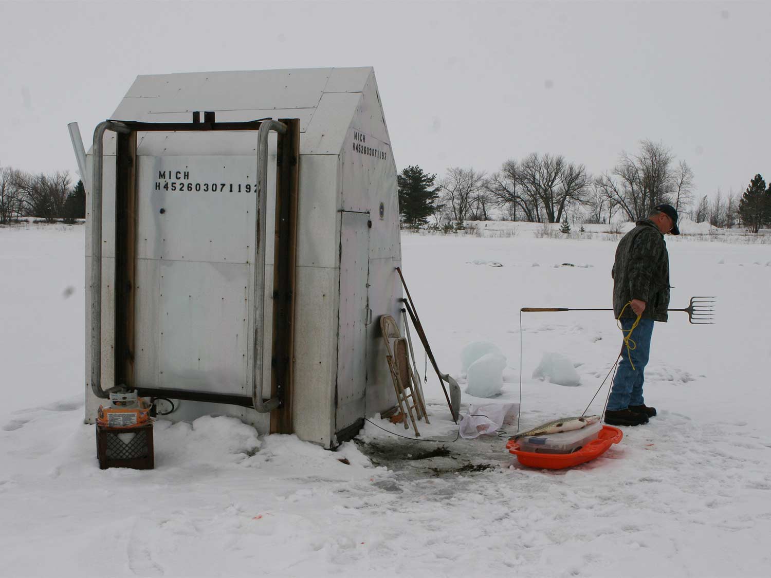 A man stands in the snow next to a shed.