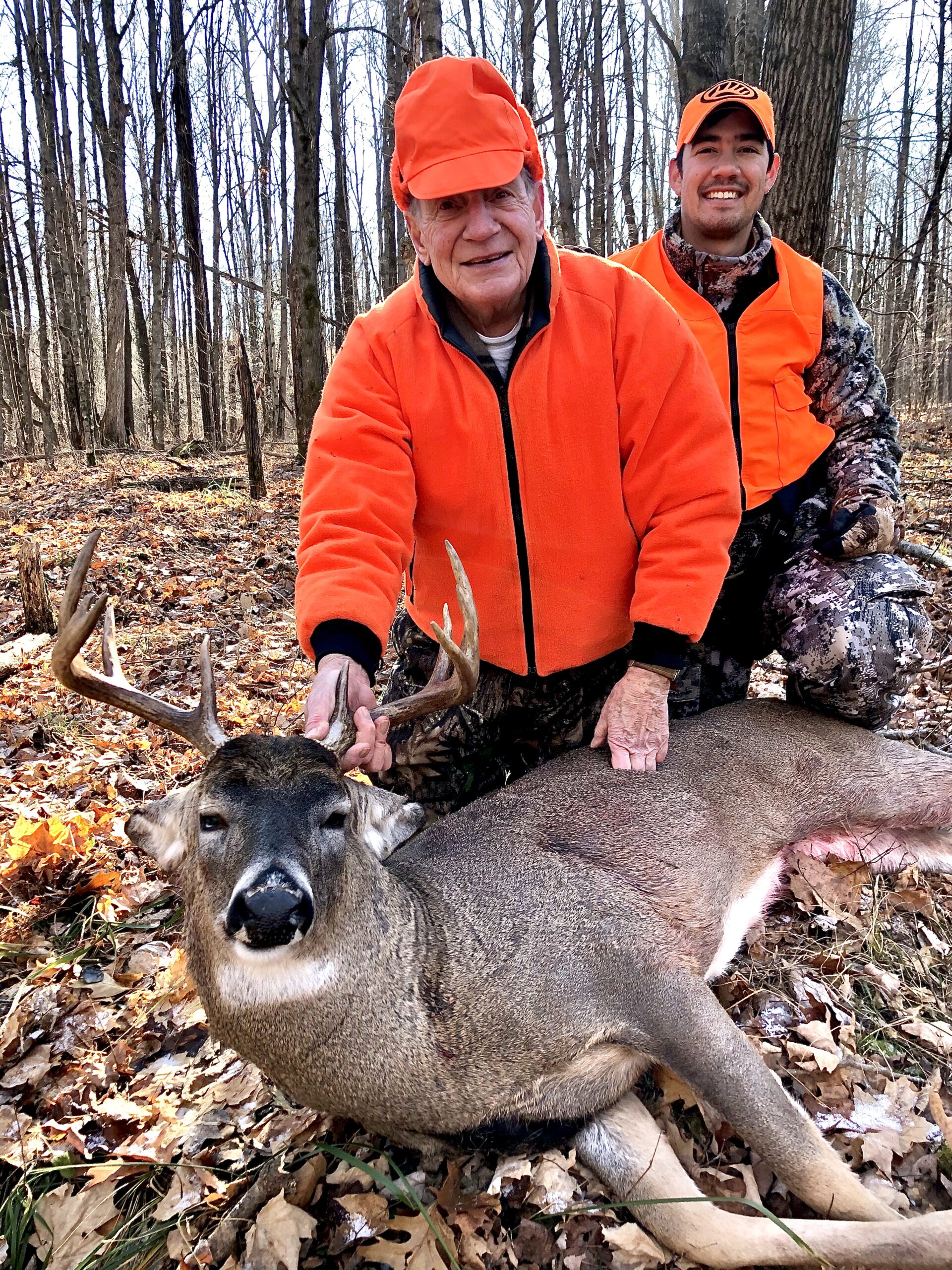 An older hunter and his grandson admire a mature Wisconsin buck in the fall deer woods.