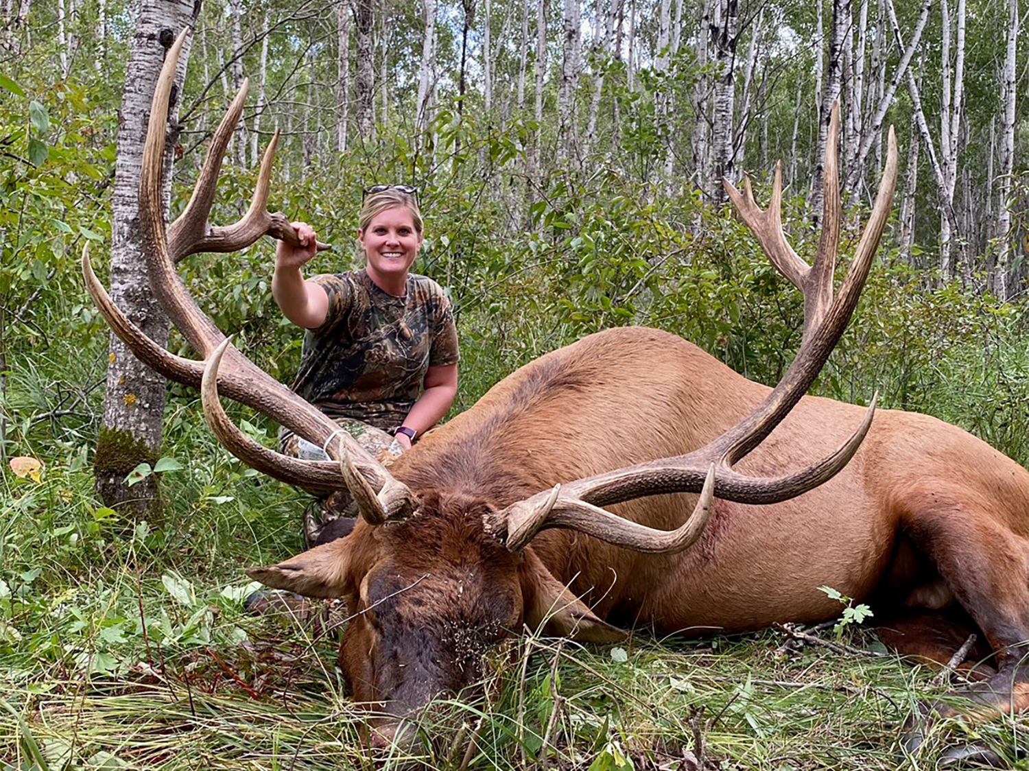 A woman kneels behind a large elk.
