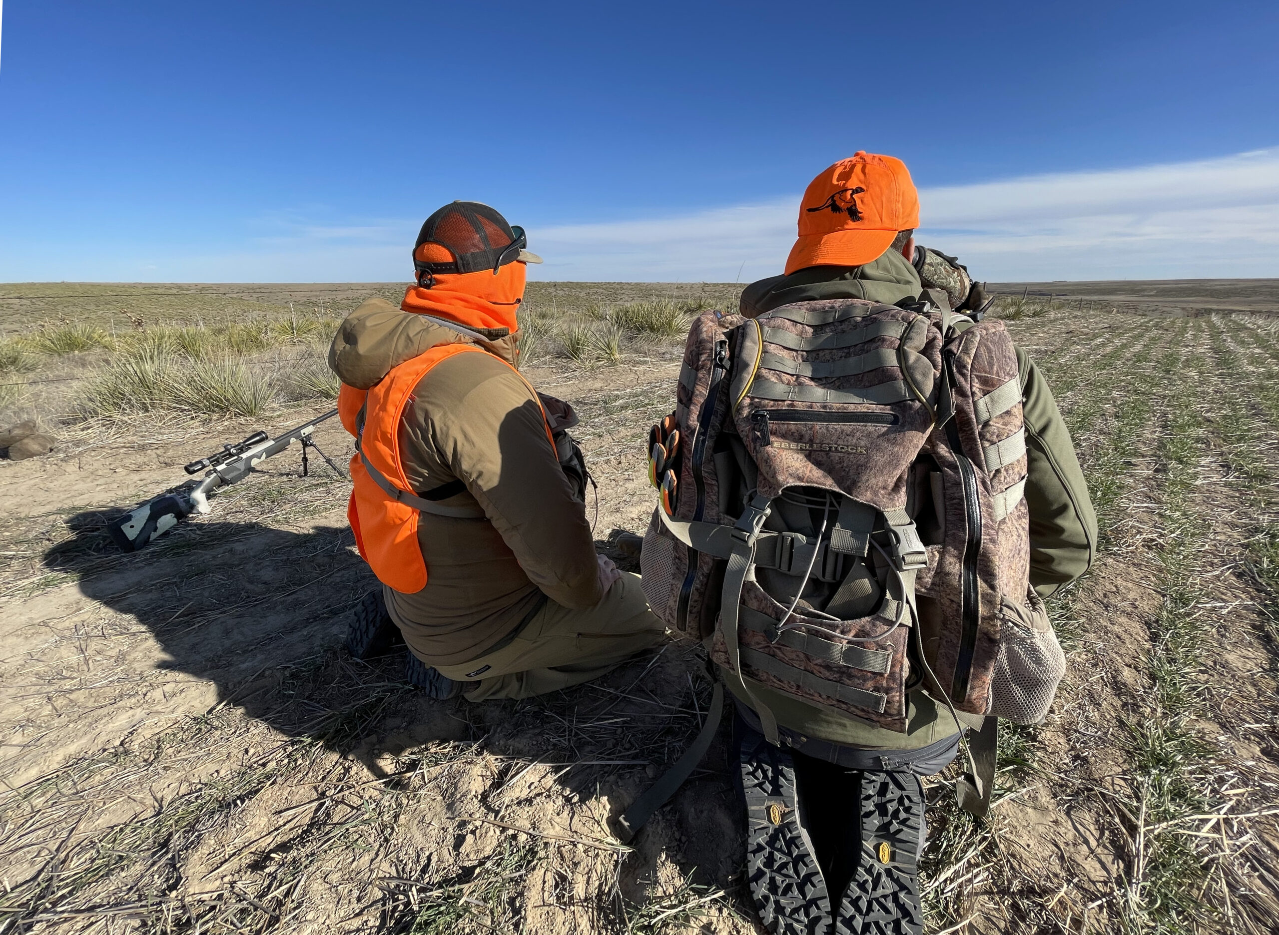 Two hunters kneel beside a rifle as they glass for deer in Eastern Colorado.
