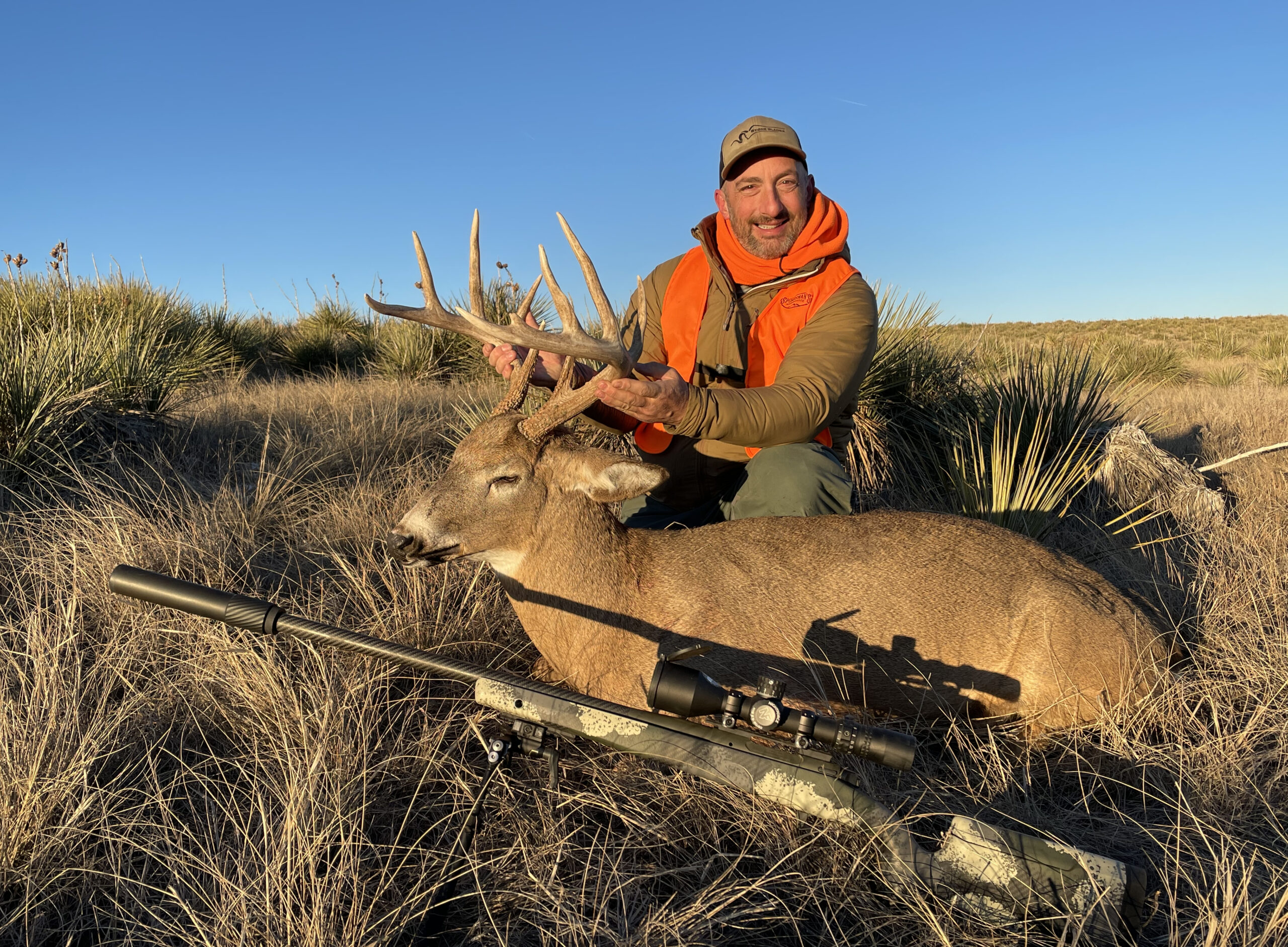 A hunter holds the antlers of a big Colorado buck, a Springfield Waypoint rifle resting on a bipod in front of them.