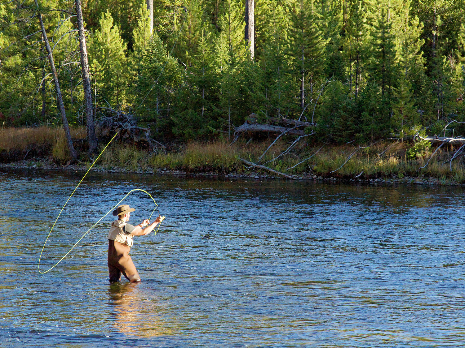 An angler wades through a river while flyfishing, wearing the best fishing vest.