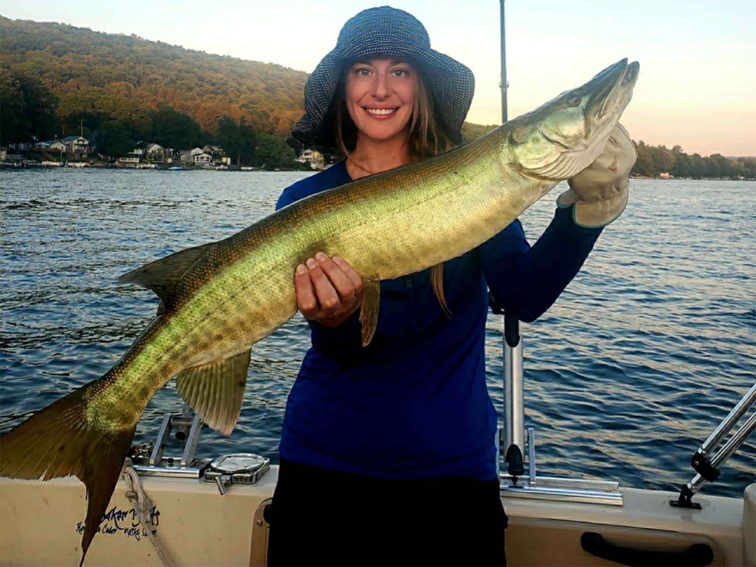 A woman smiles and poses while holding a large muskie fish.
