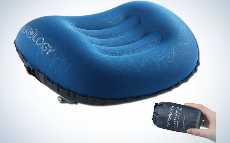 A blue and black pillow with an oval shape and deeper in the middle where the head will be supported, as well as a human hand which holds the packing bag of this pillow.