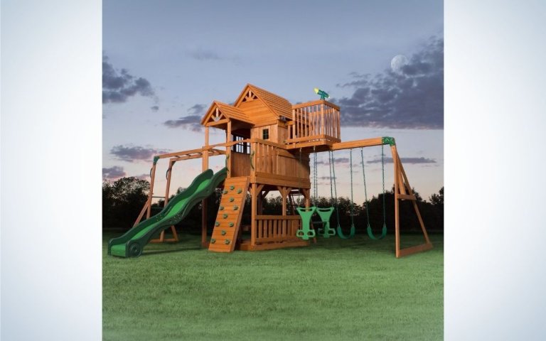 A playground with wooden spaces and mini rooms, with some small steps to climb next to it and four slides and a green slide.