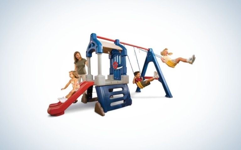 A mother and three children playing in a playground outside, with a metal structure and a red slide, and two yellow sliders.