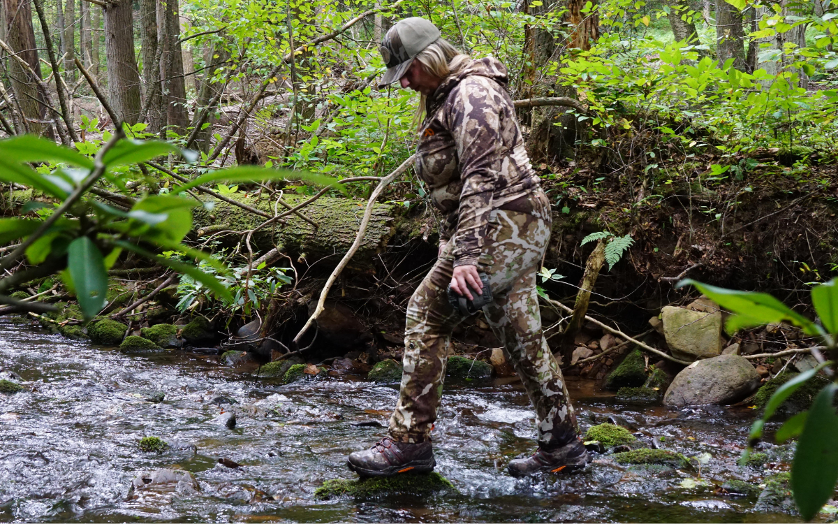 A woman wearing the Muck Alpha Pursuit boots crosses a creek.
