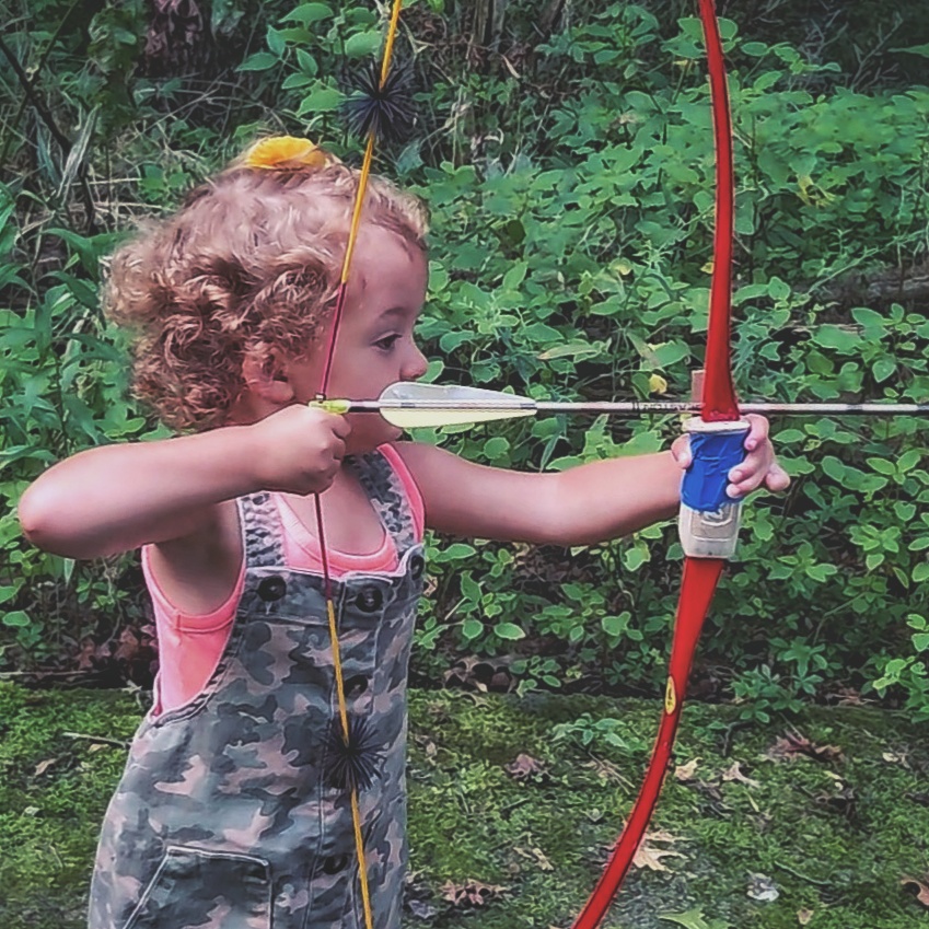 A little girl shoots a red Bear bow.