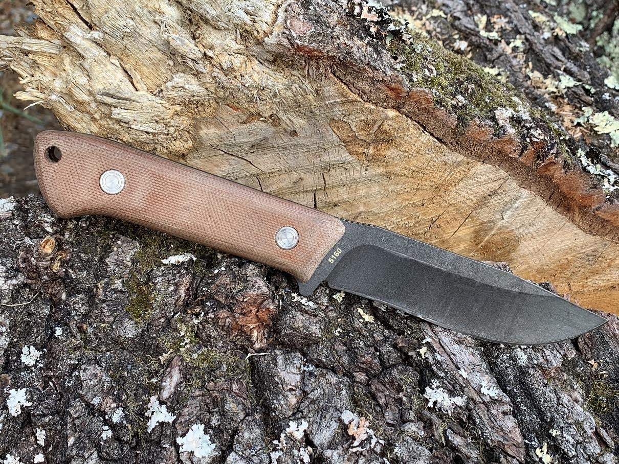 A bushcraft knife with a wooden handle laying on a stump