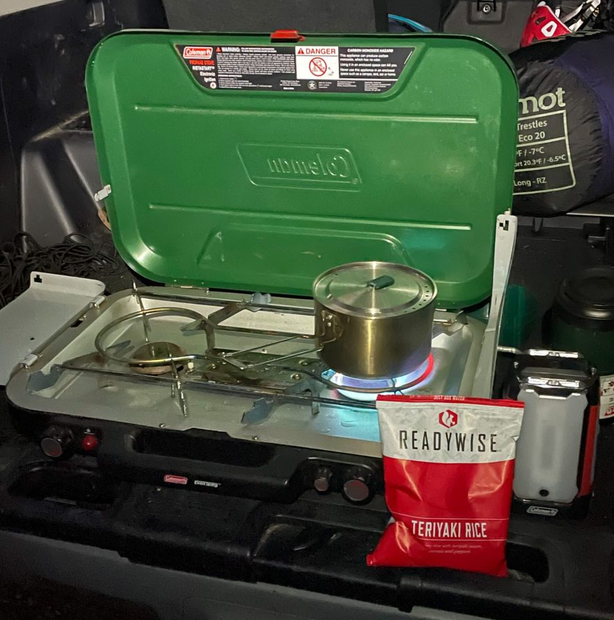 A green Coleman stove cooking a ReadyWise teriyaki meal