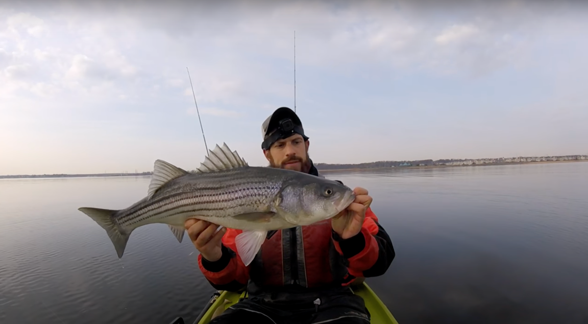 A man in a kayak wearing a red jacket holds a large fish
