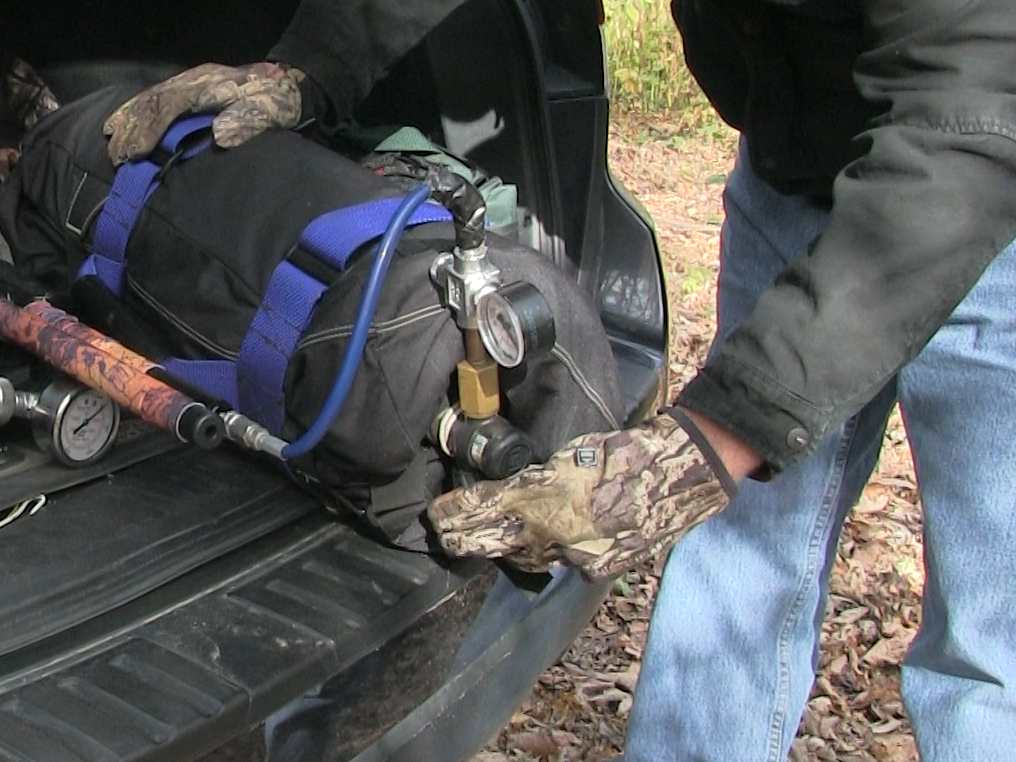 A man filling his air rifle with air in the back of his car