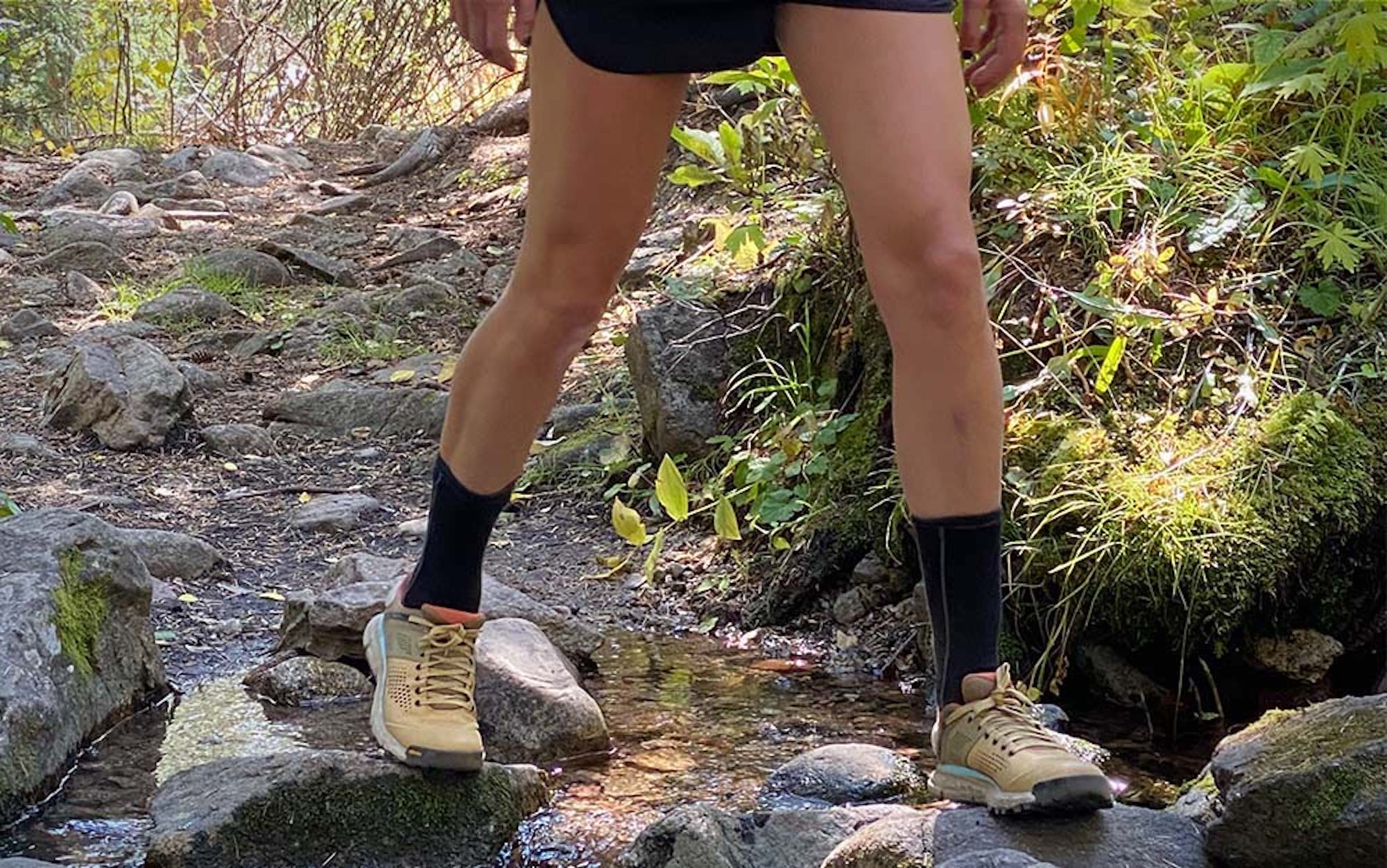 A woman’s legs crossing a stream wearing yellow low hiking shoes.