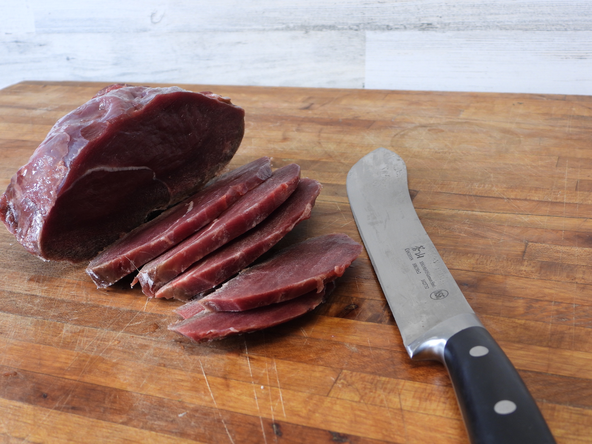 Slices of raw meat on a wooden cutting board next to a knife