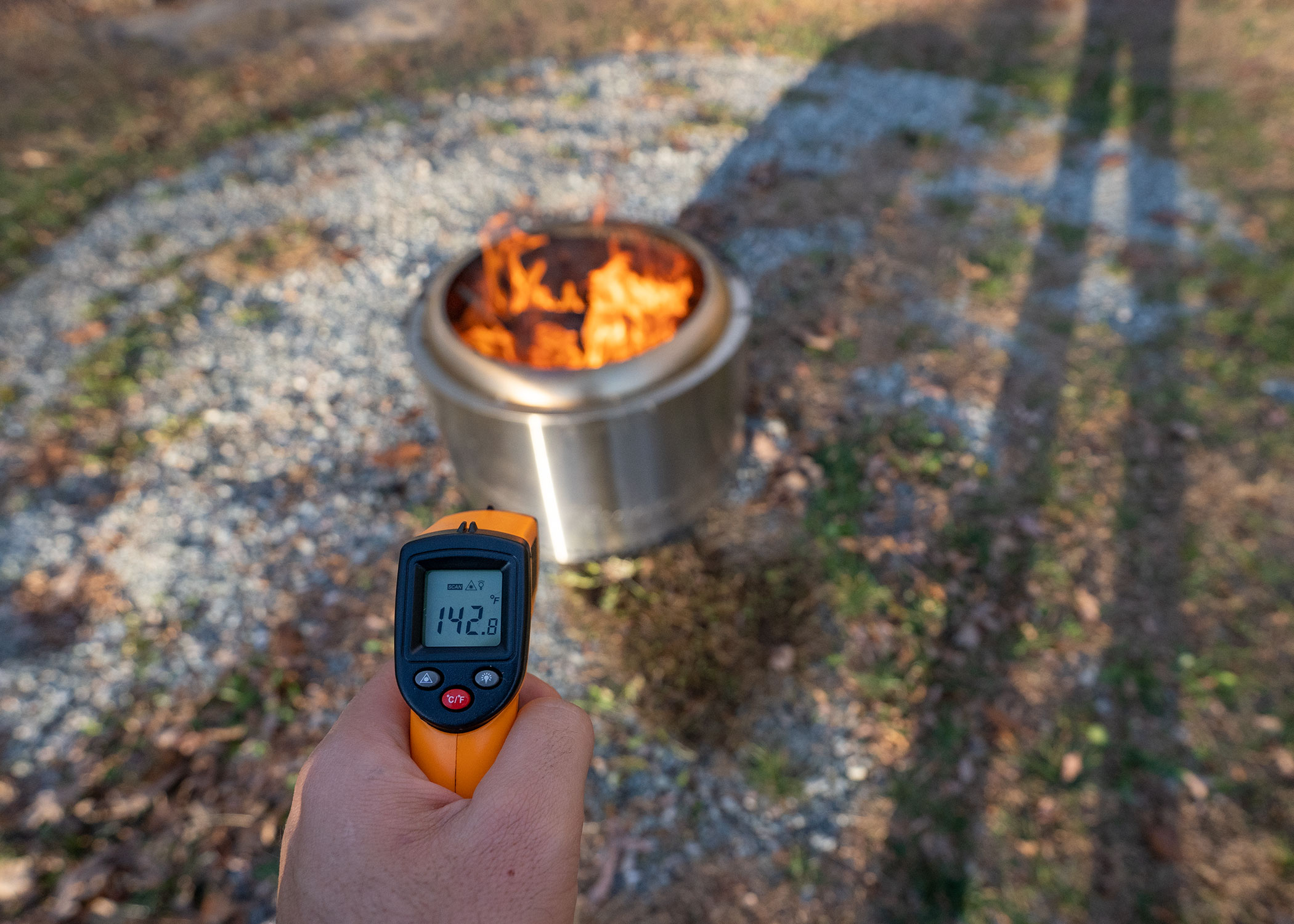 A hand holding a laser thermometer over a fire pit