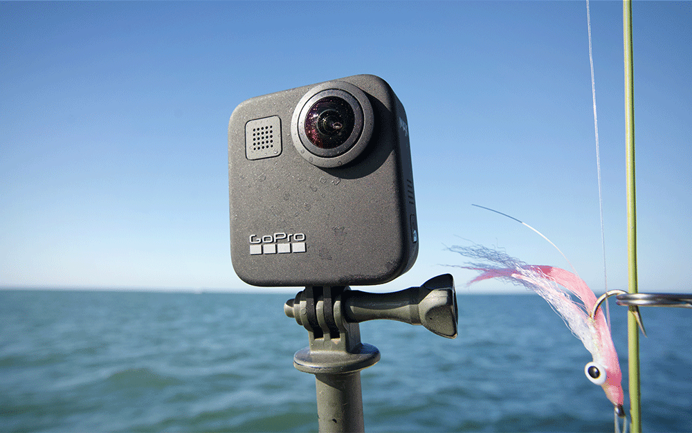A small black camera mounted on a tripod next to a fishing rod and fly over the ocean
