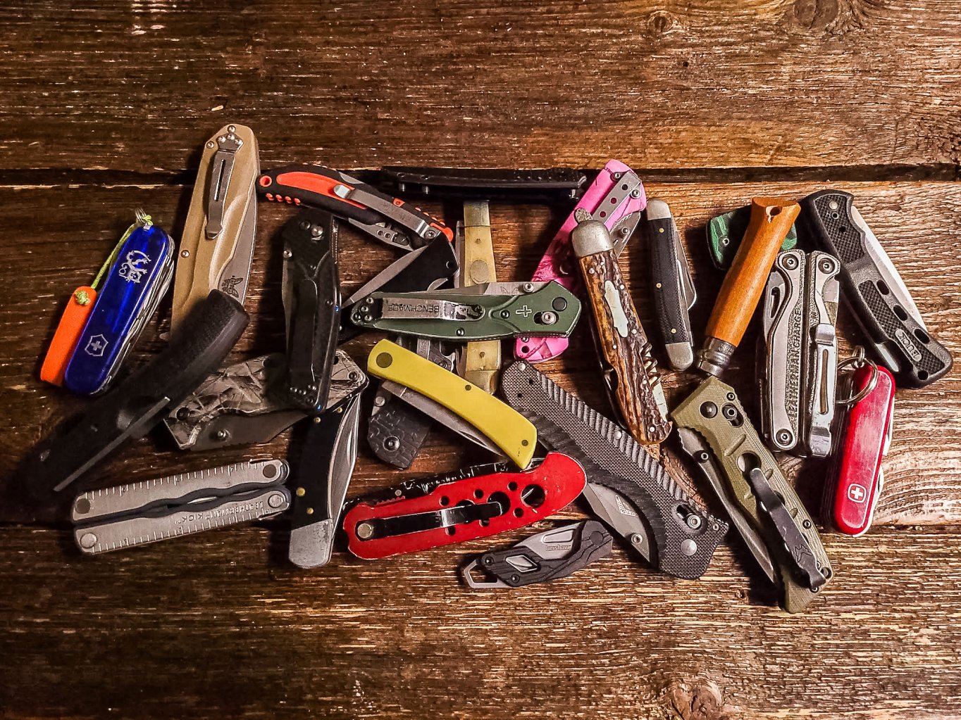 A pile of pocket knives on a wooden surface
