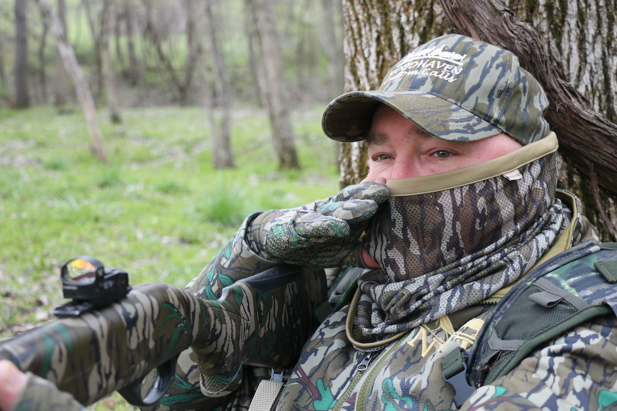 A man using a turkey mouth call dressed in camo