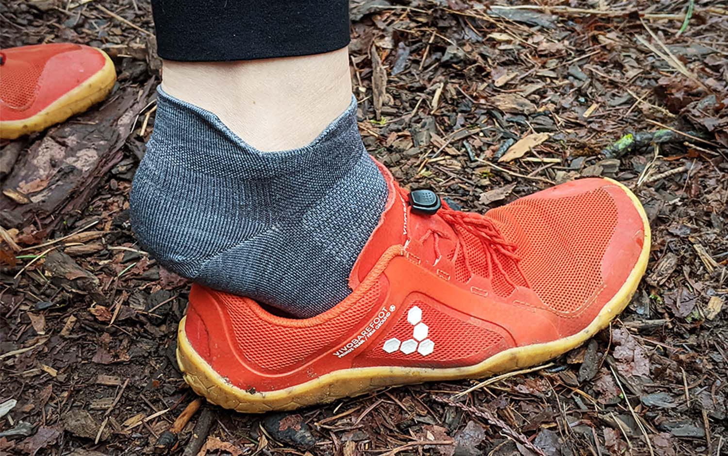 Feet wearing low grey hiking socks putting on orange hiking shoes