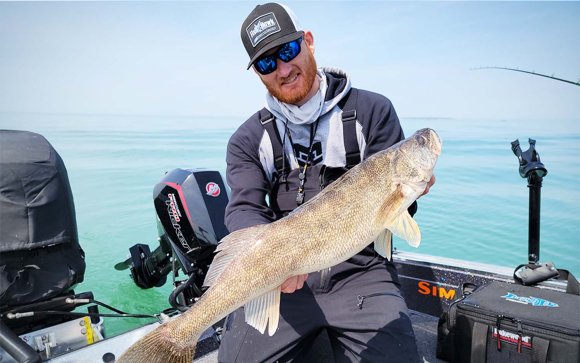 A man holding a walleye on a boat