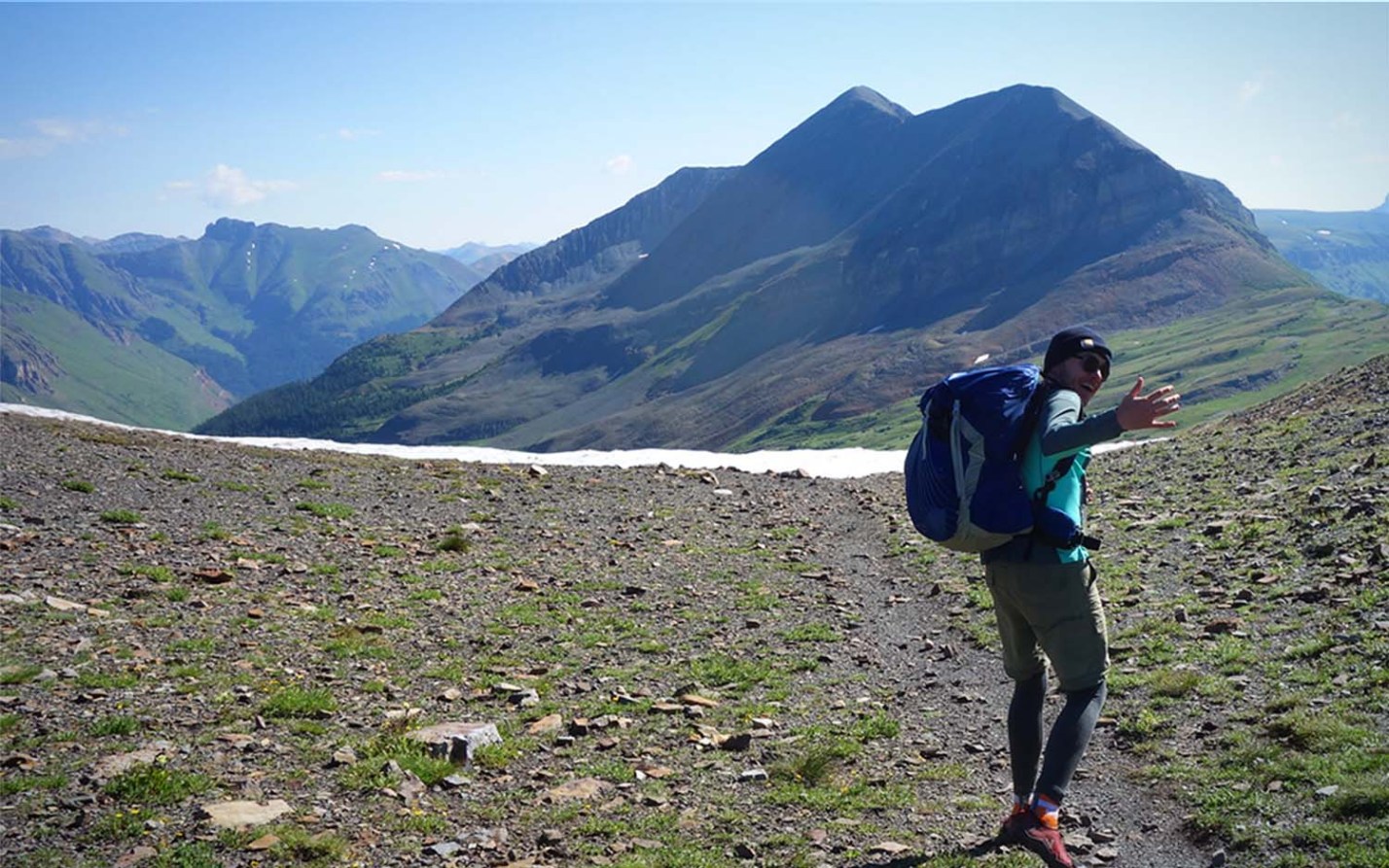 A man wearing a best backpack walking through a field with mountains in the background