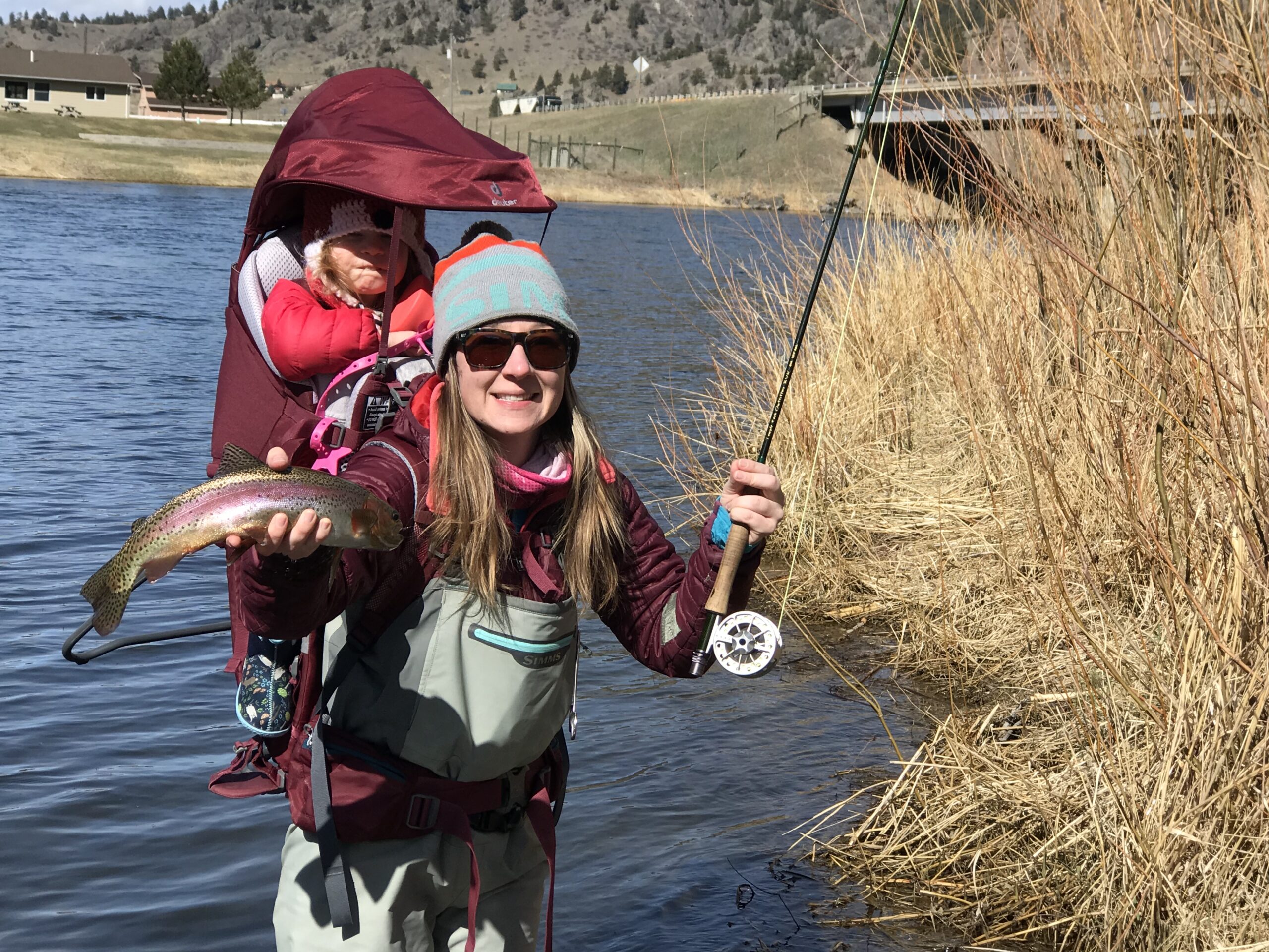 A woman fishing with a toddler in a red backpack