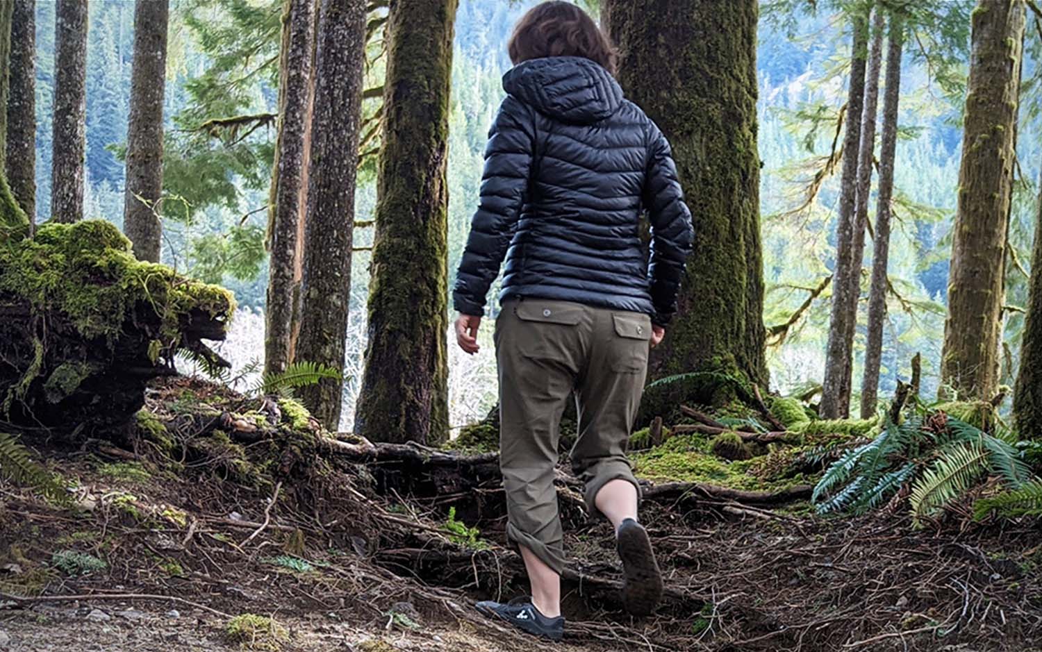 A woman walking through the woods wearing brown best hiking pants