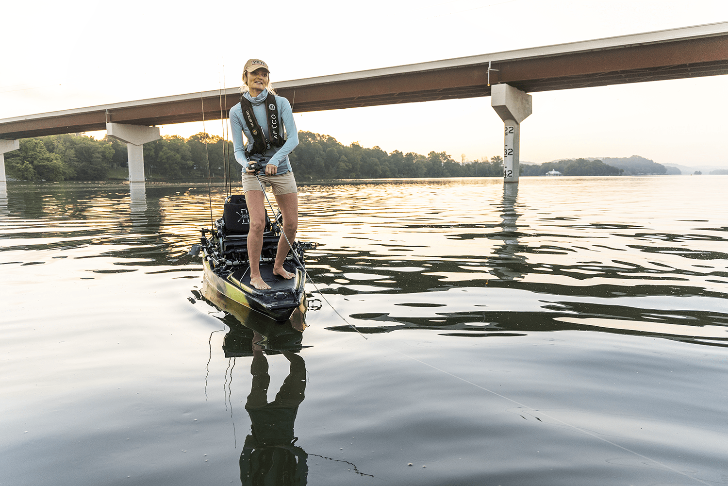 Fischer casts from kayak in front of bridge