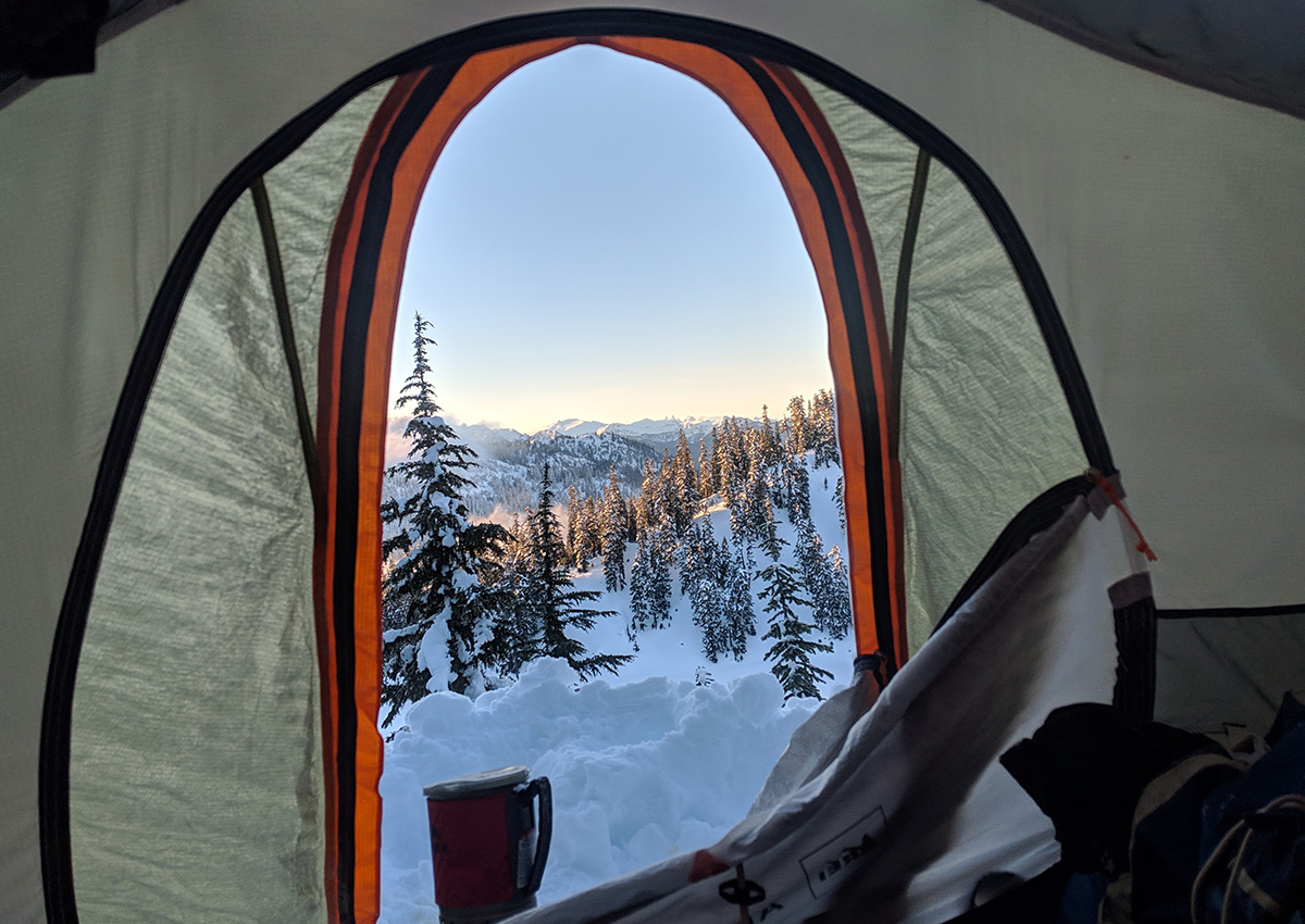 A tent door is open exposing a beautiful snowy view.