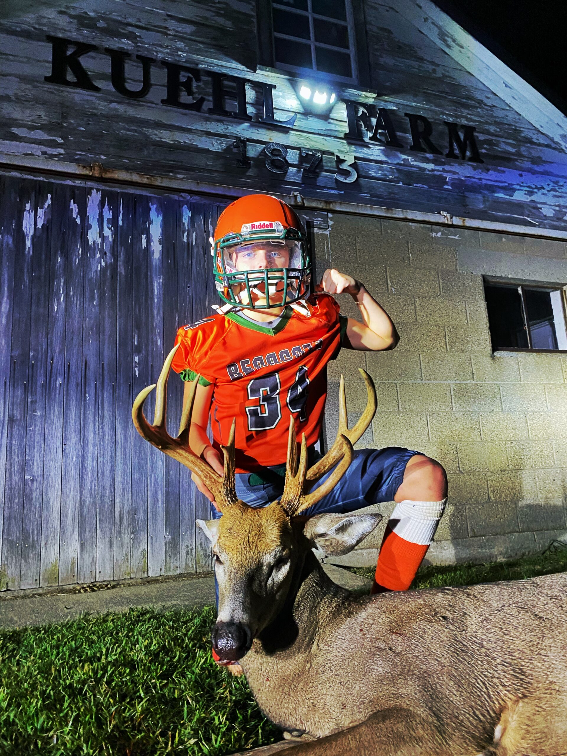 A young football player flexes next to a nice Indiana buck.