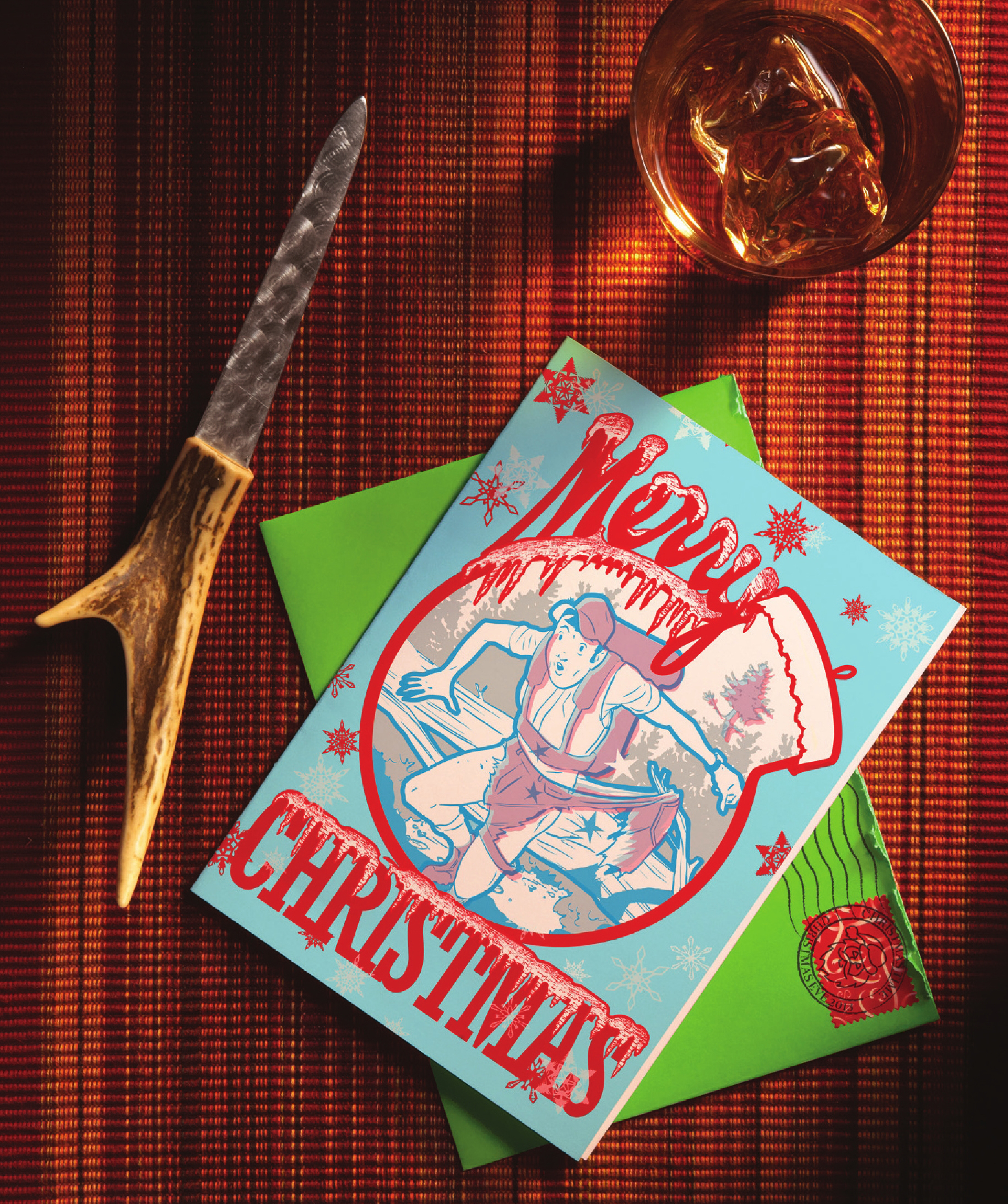 A Christmas card of a hunter with torn pants on a red cbackground with an antler letter opener
