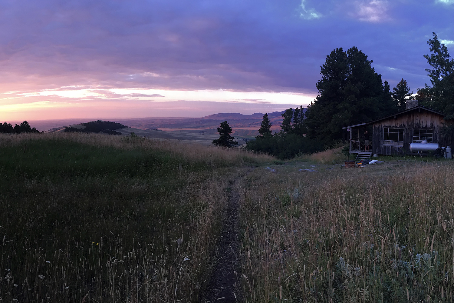 sunset over meadow with cabin to side