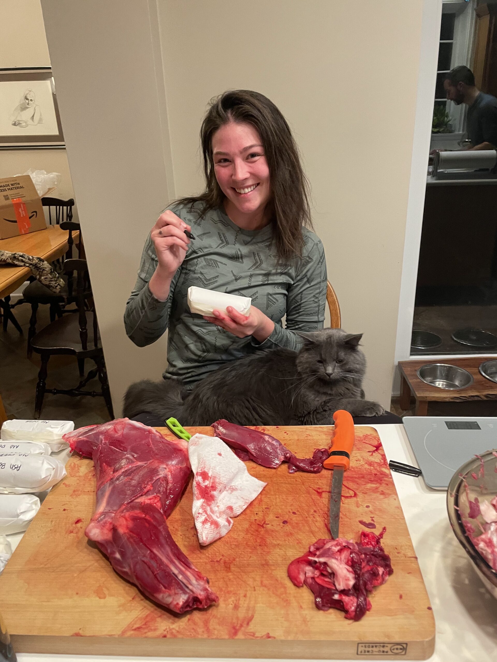 Fenrir the cat assists Thess in labeling cuts of meat for the freezer.