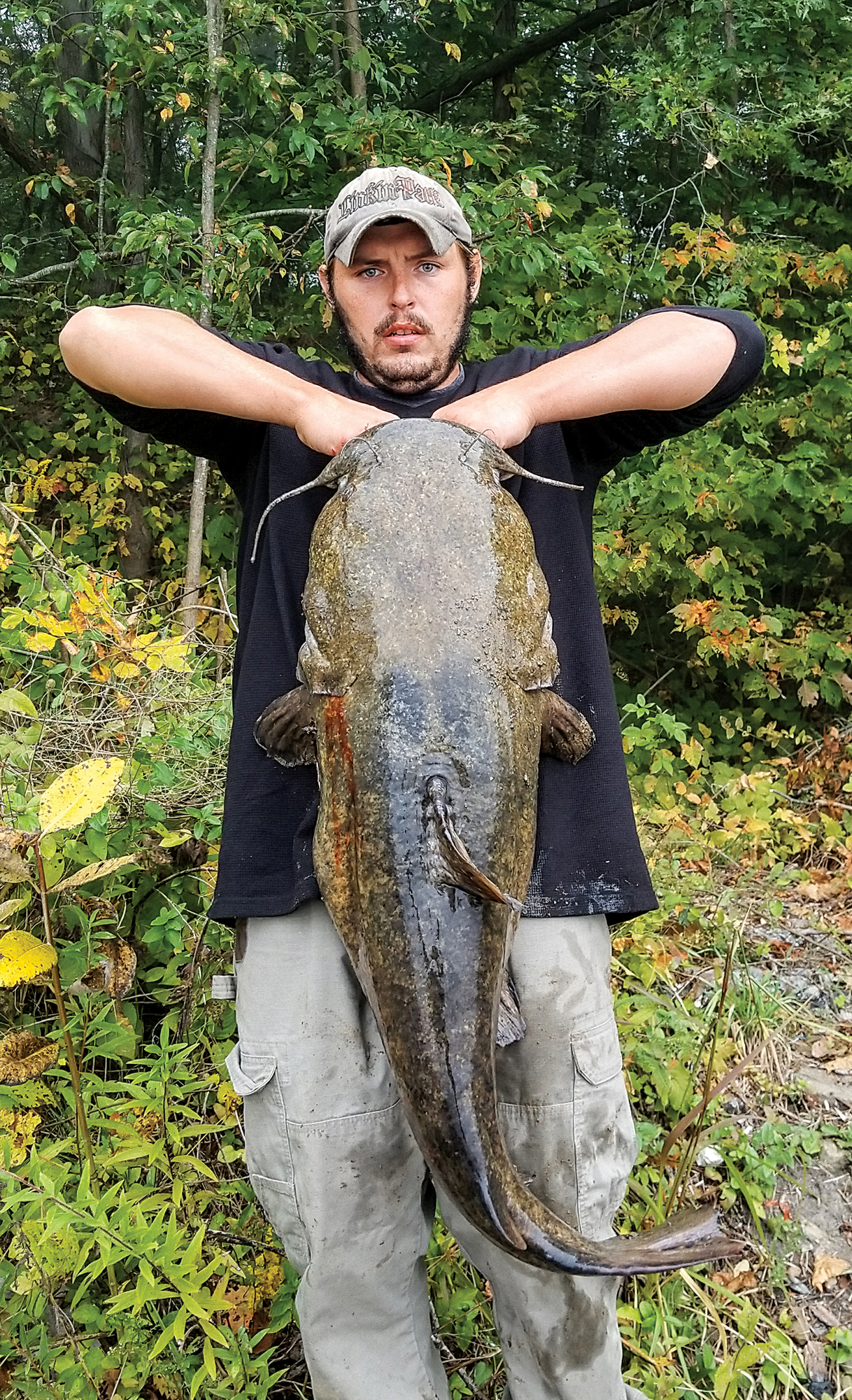 A man holds up a big flathead catfish.