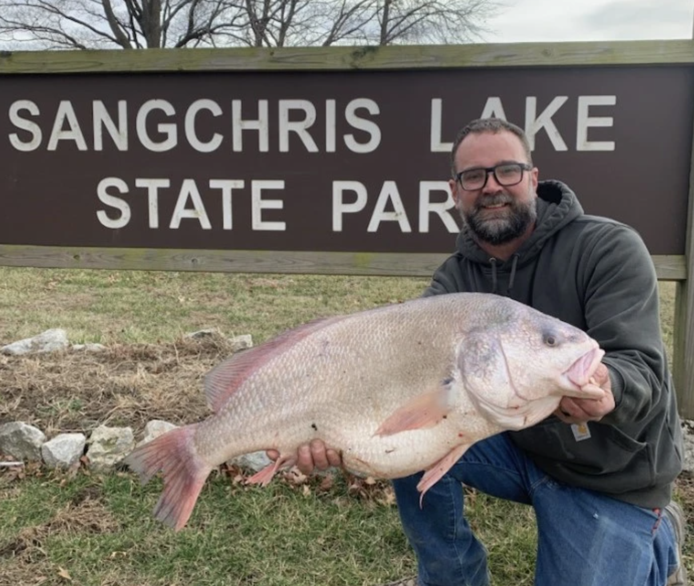 A man holds a freshwater drum in front of a state park sign.
